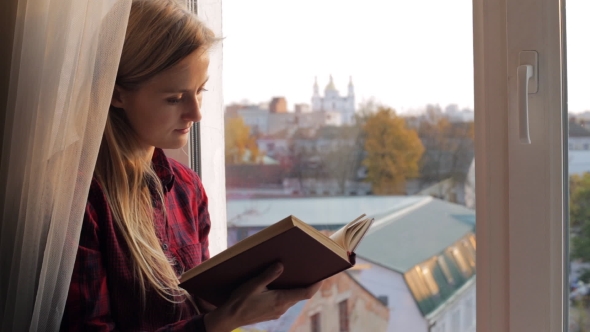Happy Woman Reading Book Near the Window on Sunset