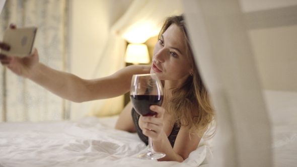 Sexy Woman Drinks Wine and Takes Selfie on Bed