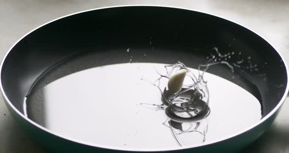 Cook throws garlic in sunflower oil on a frying pan, side view. Slow movement