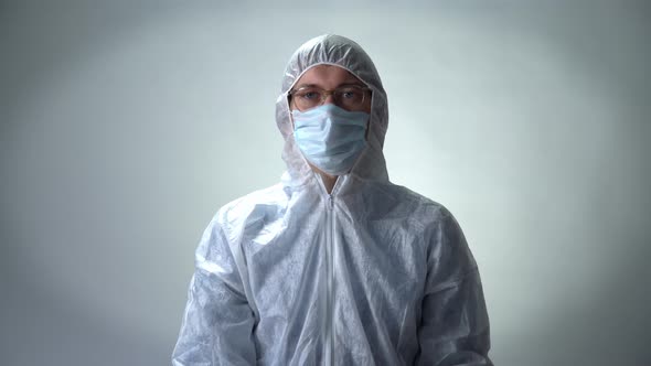 Serious Man in a Protective Suit, Medical Mask and Glasses Shows a Heart of Roses on White