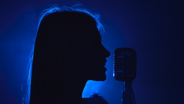 Girl Sings in a Retro Microphone. Smoke Background. Silhouette. Side View. alt