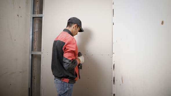 Construction Worker Is Installing a New Drywall in the Apartment Wearing Uniform. alt