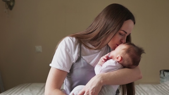 Happy Mother Holding a Baby in Her Arms and Gently Kisses