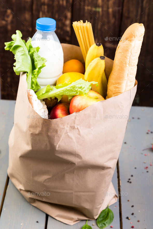 Grocery shopping concept. Different food in paper bag on wooden background.