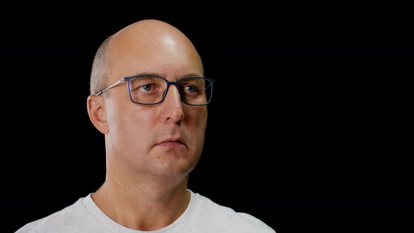 Face Bald Man in Glasses, White T-shirt on Black Background. Portrait Serious Man in Glasses Looking alt