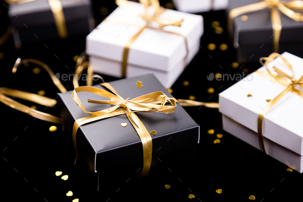 Black and white gift boxes with gold ribbon on shine background. Close up.