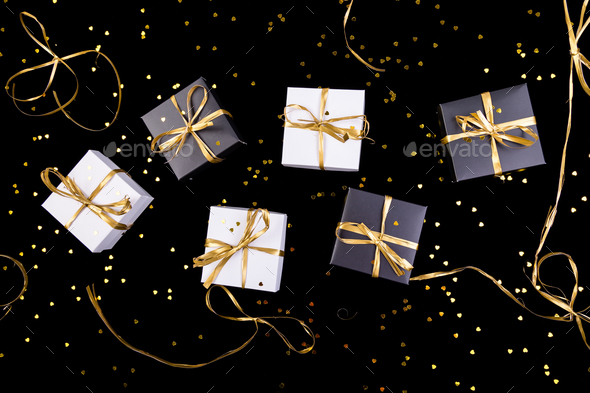 Black and white gift boxes with gold ribbon on shine background. Flat lay.