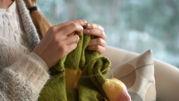 Young Woman Knitting Warm Wool Sweater in the Sitting Room Against Snow Landscape From Outside. alt