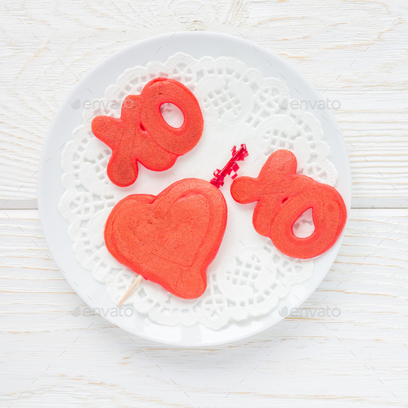 Red velvet pancakes with xo sign, hugs and kisses, and heart on white plate, top view, square