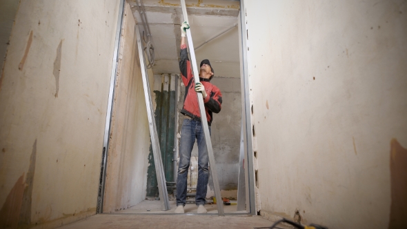 The Builder in Gloves Installs a False Wall, the Man Uses Metal Profiles To Create a Gypsum alt