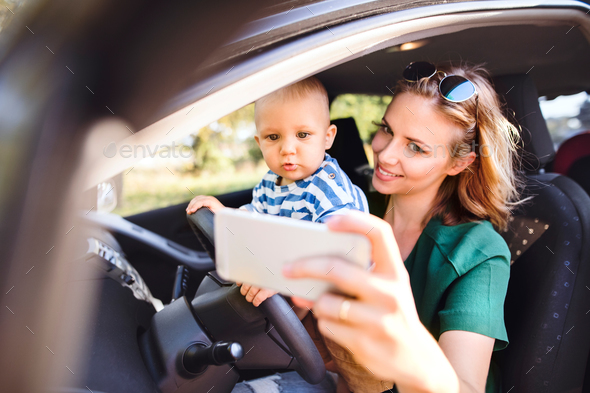 Young mother with smartphone and baby boy in the car.