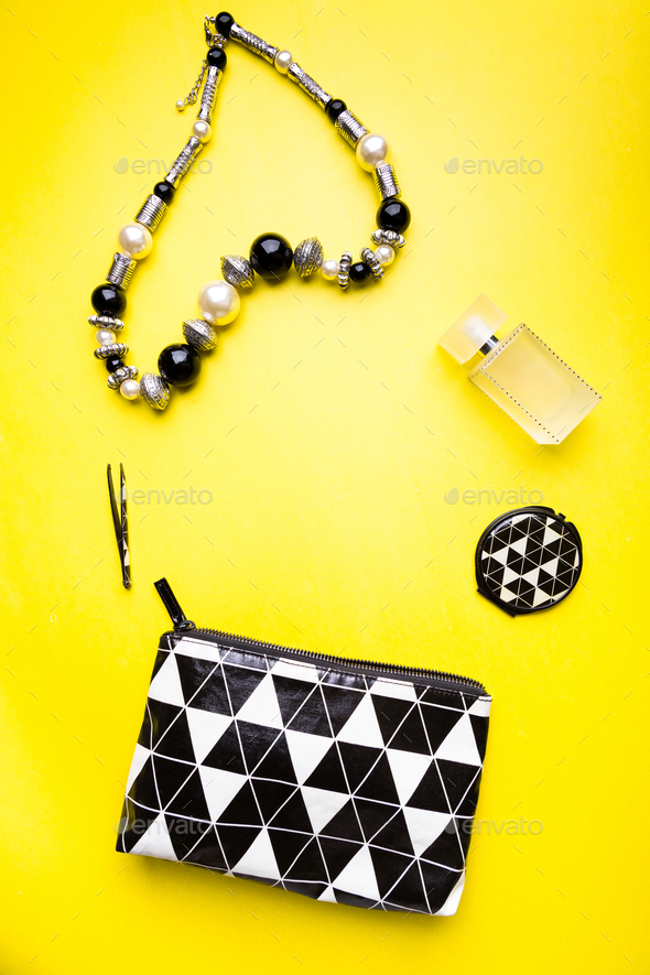 Woman handbag with makeup and accessories on yellow background. Flat lay.