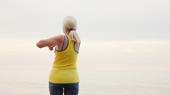 A Middle-Aged Woman Warms Up on the Beach. Early Morning alt