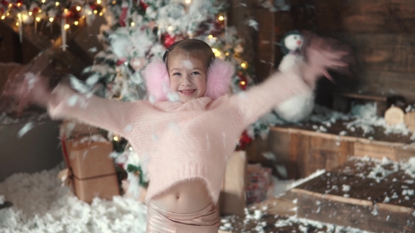 Christmas or New Year. Portrait of a Little Girl in Christmas Decorations. a Child Throws Snow Up alt