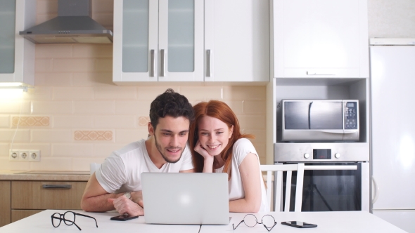 Young Business Couple Working with Laptop at Home in Kitchen. alt