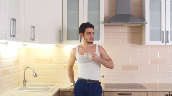 Attractive Young Man Drinking Water From a Glass in Kitchen. alt