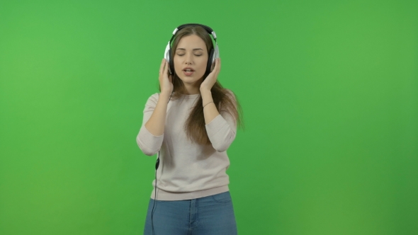 Beautiful Girl with Long Hair Listening To Music Through Headphones. On the Green Screen. She Dances