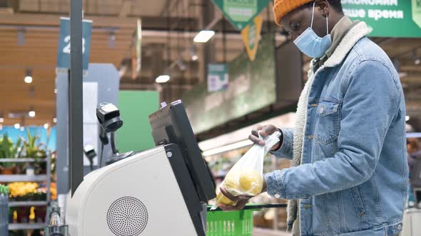 AfricanAmerican Male Customer Wearing a Medical Mask Punches Through Items at a Selfservice Checkout alt