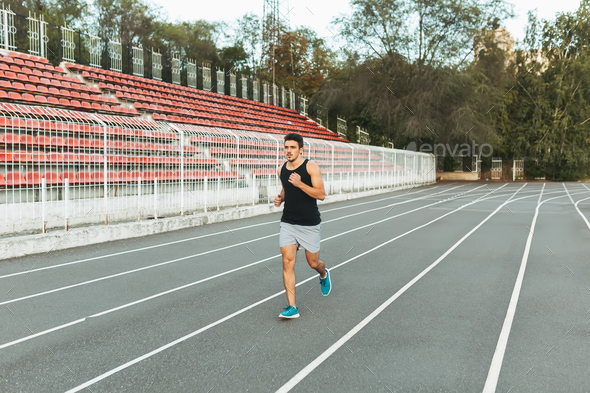 Young athletic man running on the stadium in the morning - Stock Photo - Images