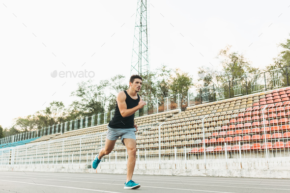 Young athletic man running on the stadium in the morning - Stock Photo - Images