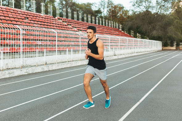 Young athletic man running on the stadium in the morning - Stock Photo - Images