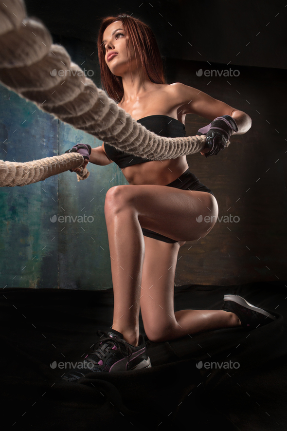 The strong young woman pulling rope at a gym