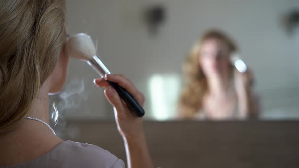 Makeup Brush for Young Woman and Powder Looking in the Mirror Young Woman Applies Makeup alt
