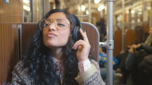 Portrait of Stylish and Fashionable Brunette Rides in a Train Car and Listens with Music on