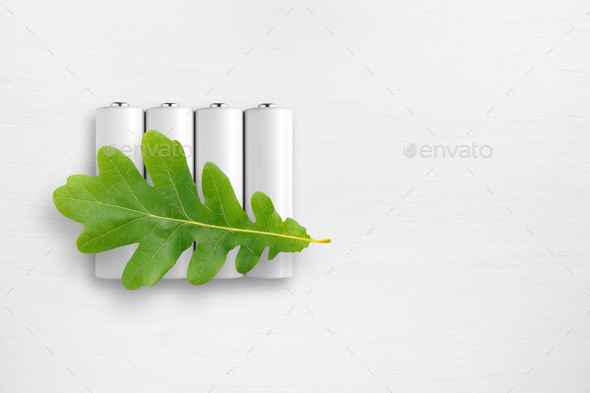 Batteries and green oak leaf on white table. Ecological energy concept.