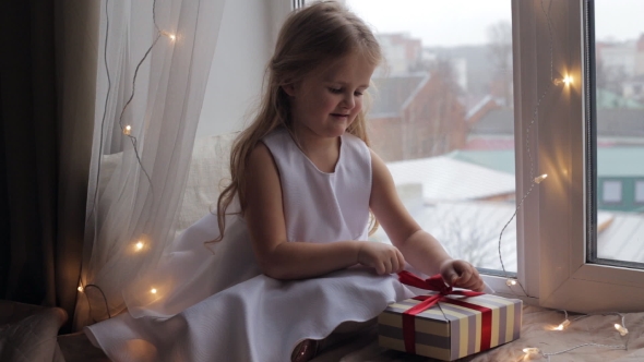 Young Girl Unpacking Her Present and Sitting on a Windowsill