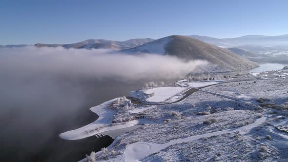 Aerial view flying over snow covered landscape next to lake alt