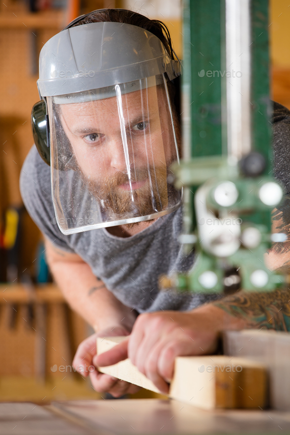 Craftsman with safety mask visor handles band saw in workshop - Stock Photo - Images