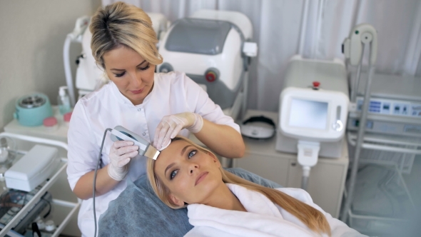 The Cosmetologist Makes the Procedure Ultrasonic Face Peeling of the Facial Skin of a Beautiful alt