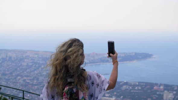 Back View of Woman Holding Smartphone and Taking Photos of Beautiful Seascape alt