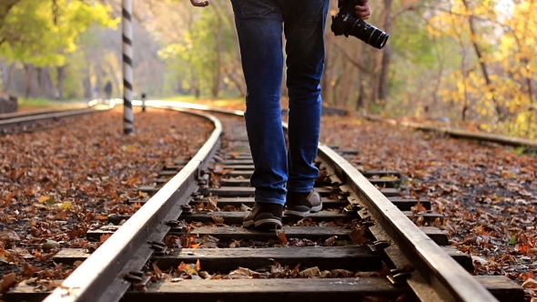 A Man with DSLR Camera Walks Down Train Tracks on a Background Autumn Forest. A Man Departs From the