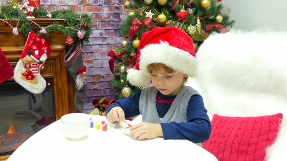 Boy in a Santa Hat Is Painting a Christmas Toy