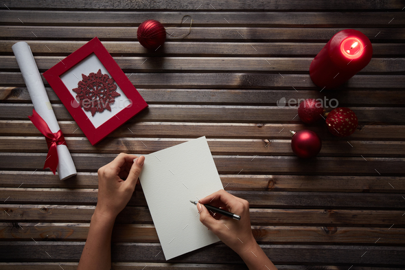 Human writing xmas wishes on blank paper sheet with holiday symbols near by Human writing xmas wishes on blank paper sheet with holiday symbols near by