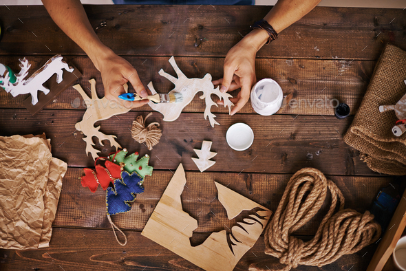 Craftsman painting wooden deers with white gouache Craftsman painting wooden deers with white gouache