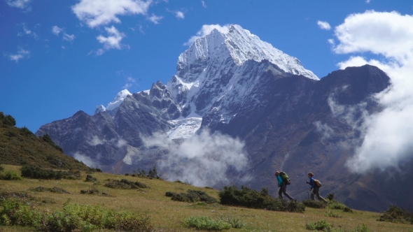 Girls with Backpacks Climb the Mountain Slope in the Himalayas alt