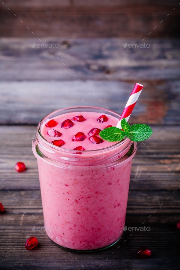 Pink pomegranate smoothie in a glass jar with mint and fresh seeds ...