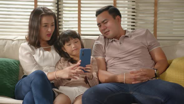 Asian Family mom and dad having fun tickling their cut little girl sitting on a couch