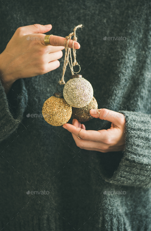 Woman in grey sweater holding decorative golden balls in hands - Stock Photo - Images