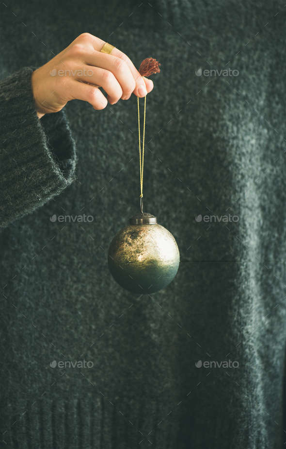 Woman in grey sweater holding decorative golden ball in hand - Stock Photo - Images