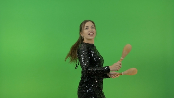Beautiful White Girl in a Black Shiny Dress. Have Fun and Dance with Maracas. On a Green Background. alt