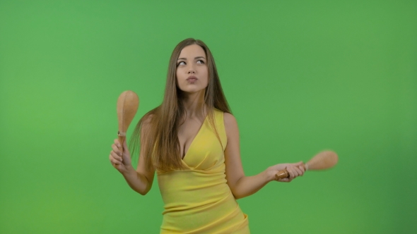 Young Beautiful Girl with Long Hair Dancing with Maracas. Fun and Cheerful, on a Green Background.