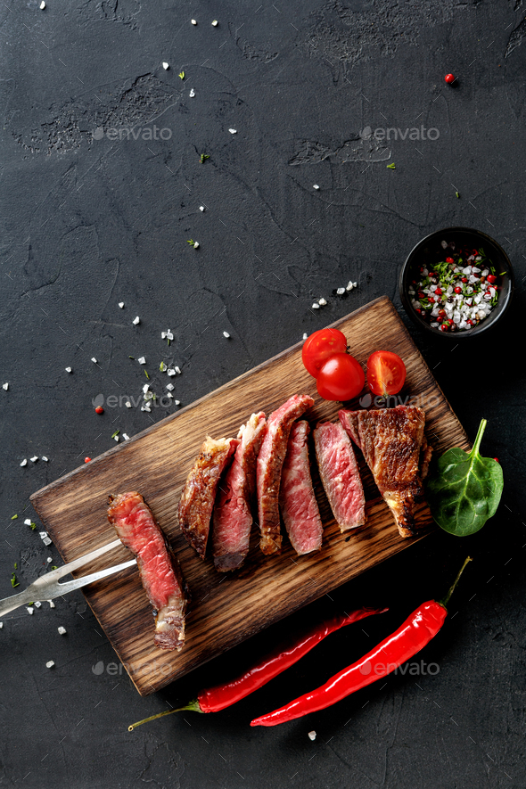 Rib eye steaks and spices on wood at black background - Stock Photo - Images