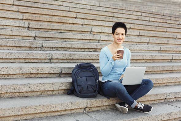 Smiling woman sitting on stairs using laptop - Stock Photo - Images