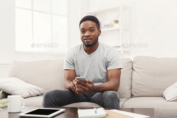 Smiling young man at home messaging on mobile - Stock Photo - Images