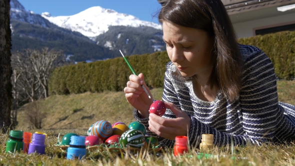 Woman Lies on the Grass and Paints Easter Eggs