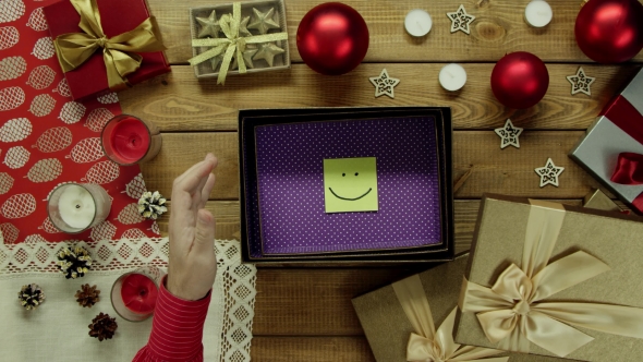 Top Down Shot of Man Opening Christmas Present Box with Sticky Note with Smile Inside